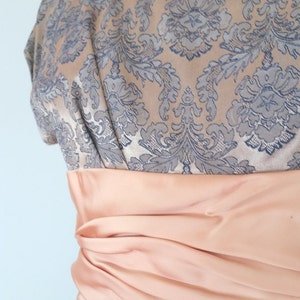 May include: A vintage dress with a floral pattern in shades of gray and peach. The dress has a fitted bodice and a full skirt. A peach-colored satin sash is tied around the waist.