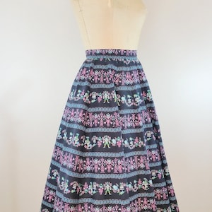 K&ouml;nnte beinhalten: Ein schwarzer Midirock mit einem bunten floralen und geometrischen Muster. Der Rock ist weit und hat eine geraffte Taille.
