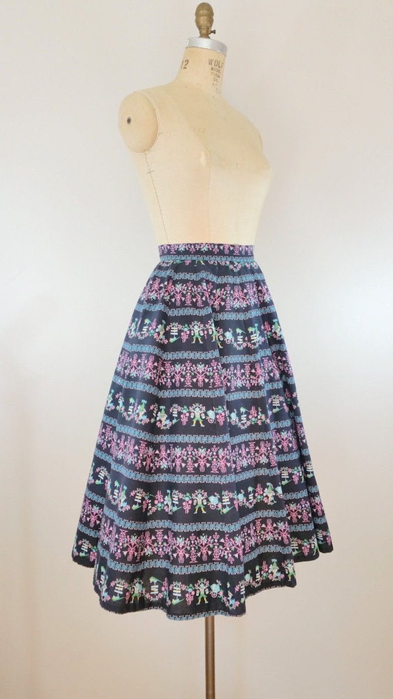 K&ouml;nnte beinhalten: Ein schwarzer Midirock mit einem bunten floralen und geometrischen Muster. Der Rock ist weit und hat eine geraffte Taille.