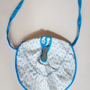 May include: A white baby bib with a blue floral pattern and blue trim. The bib has two blue ties.