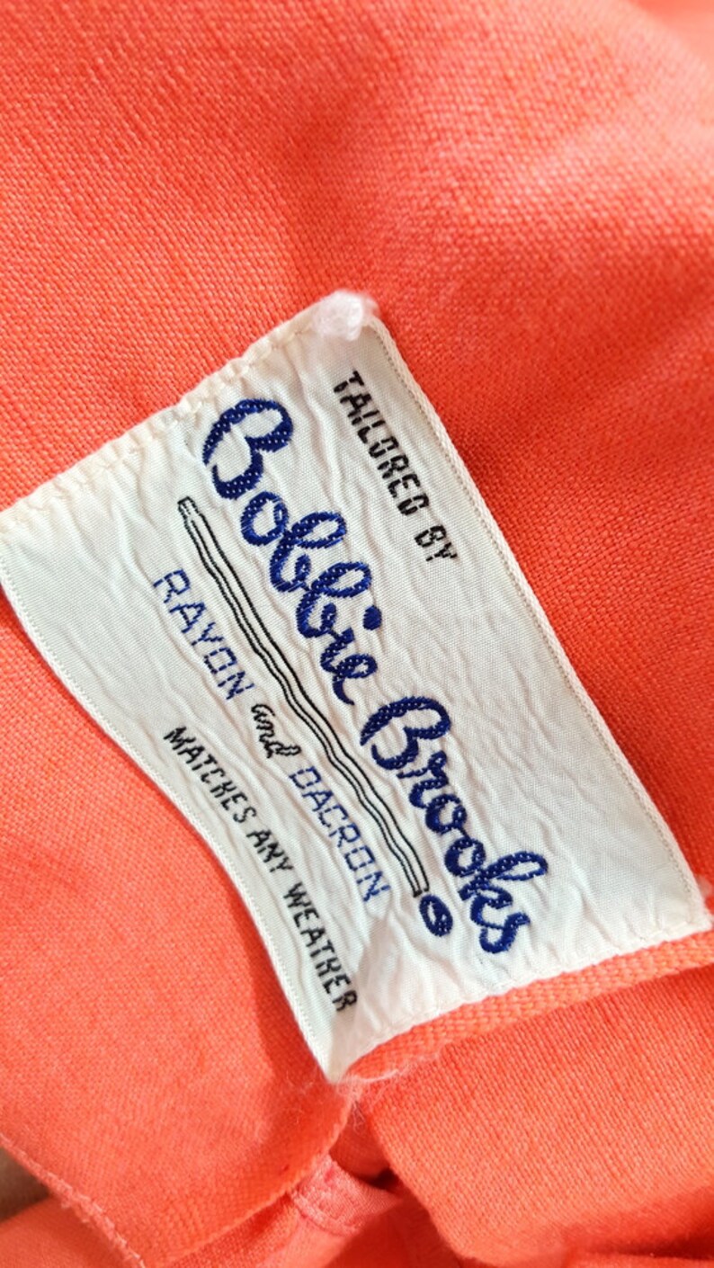 Puede incluir: Etiqueta blanca con texto azul que dice "Tailored by Bobbie Brooks Rayon and Dacron Matches Any Weather"