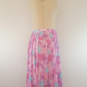 May include: A pink pleated skirt with a floral print featuring pink, blue, and white flowers. The skirt is on a dress form.