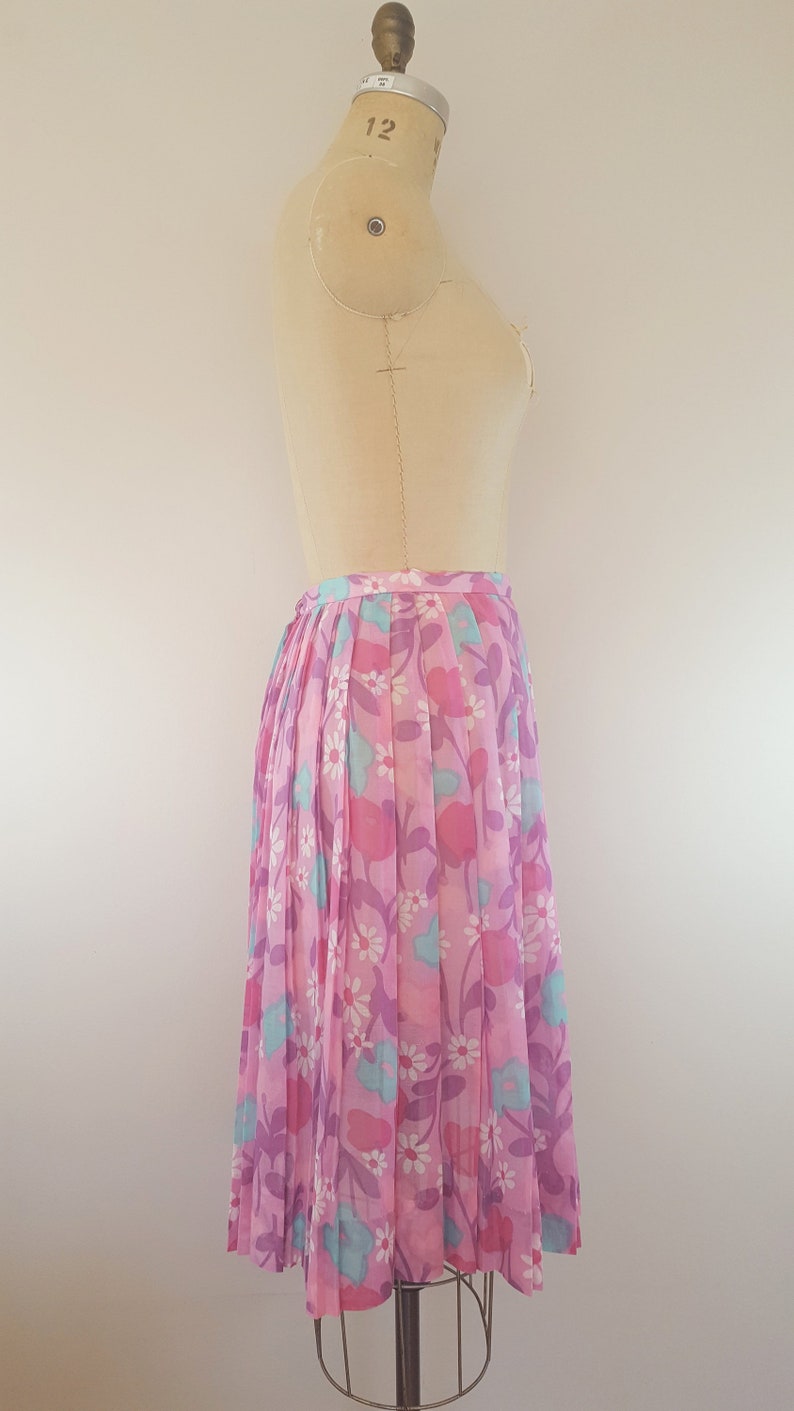 May include: A pink pleated skirt with a floral print featuring pink, blue, and white flowers. The skirt is on a dress form.