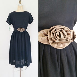 May include: A black vintage dress with a short sleeve and a brown satin rose accent at the waist.