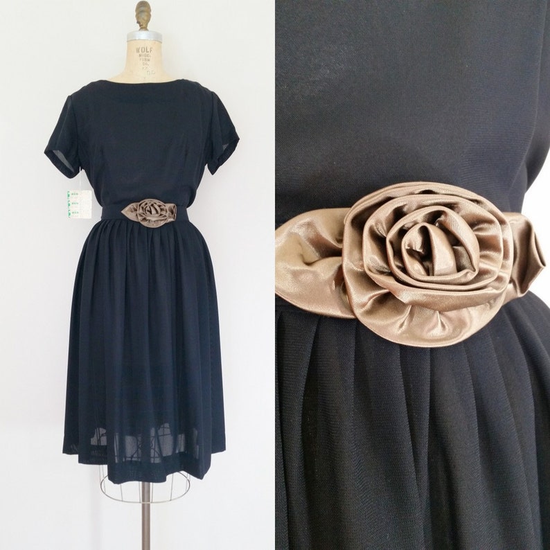 May include: A black vintage dress with a short sleeve and a brown satin rose accent at the waist.