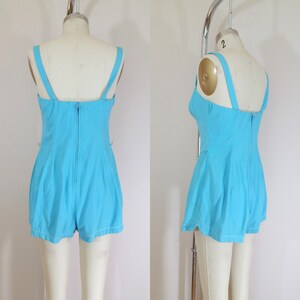 May include: A light blue one-piece swimsuit with a scoop neck and a zipper closure in the back. The swimsuit has a fitted bodice and a flared skirt.