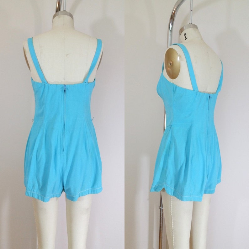 May include: A light blue one-piece swimsuit with a scoop neck and a zipper closure in the back. The swimsuit has a fitted bodice and a flared skirt.