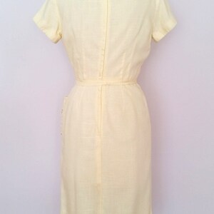 May include: A pale yellow sleeveless dress with a back zipper and a belt. The dress has a simple, classic design.