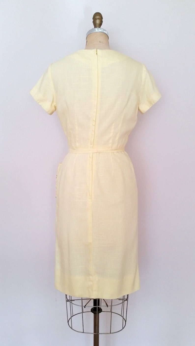 May include: A pale yellow sleeveless dress with a back zipper and a belt. The dress has a simple, classic design.