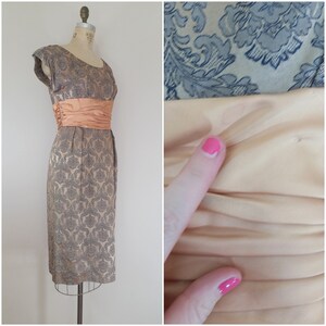 May include: A vintage 1950s or 1960s gray and silver brocade dress with a peach satin sash. The dress has a fitted bodice and a full skirt. The sash is tied in a bow at the back.