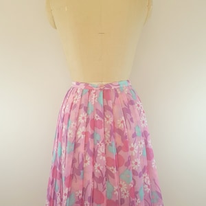 May include: A pink pleated skirt with a floral print featuring pink, purple, and blue flowers. The skirt is on a dress form.