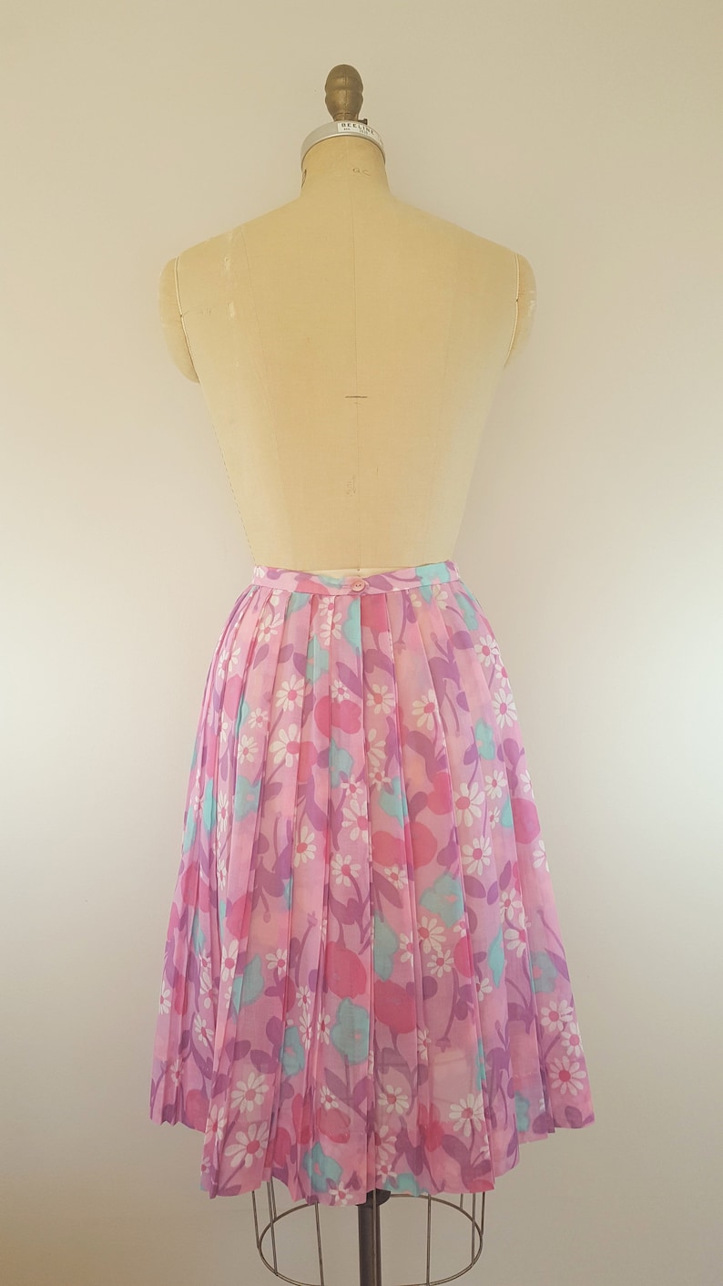 May include: A pink pleated skirt with a floral print featuring pink, purple, and blue flowers. The skirt is on a dress form.