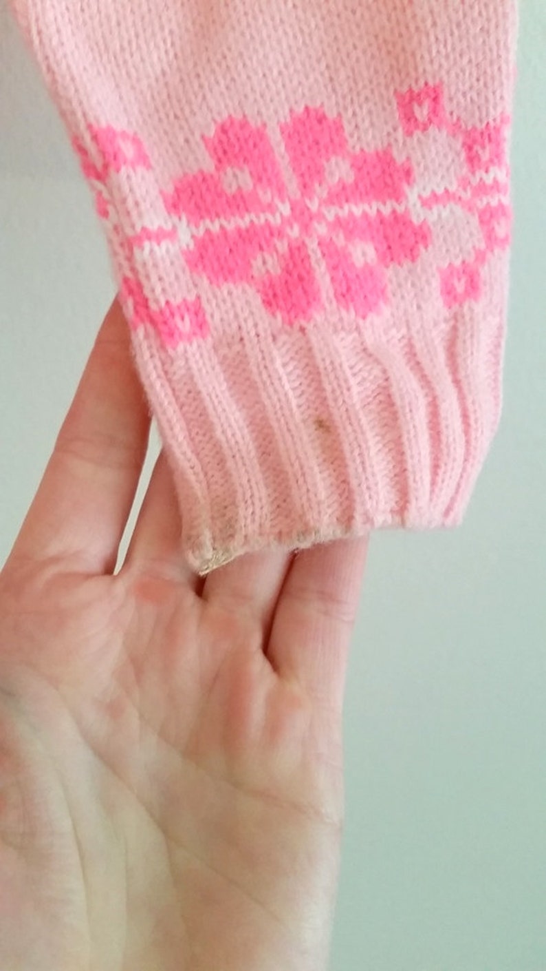 Puede incluir: Su&eacute;ter de punto rosa con un patr&oacute;n geom&eacute;trico blanco y rosa. El su&eacute;ter tiene una textura de punto de canal&eacute;.