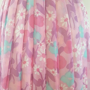 May include: A pink pleated skirt with a floral print featuring white daisies, pink and purple flowers, and light blue leaves.