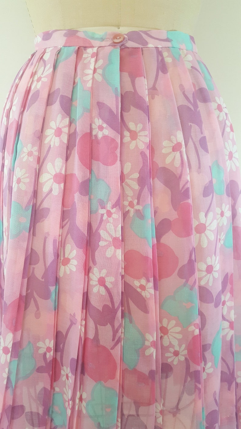 May include: A pink pleated skirt with a floral print featuring white daisies, pink and purple flowers, and light blue leaves.