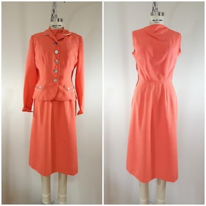 Puede incluir: Un traje de lino rosa coral con falda y chaqueta a juego. La chaqueta tiene ribetes y botones blancos. La falda es de largo hasta la rodilla.
