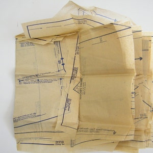 May include: A vintage sewing pattern with instructions and diagrams printed on beige paper. The pattern includes a cutting line and a fold line.