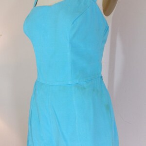 May include: A light blue sleeveless jumpsuit with a square neckline and a fitted bodice. The jumpsuit has a wide leg and a hem that falls just above the knee.