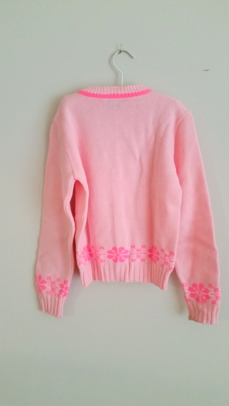 Puede incluir: Un su&eacute;ter de punto rosa con ribete rosa ne&oacute;n y un patr&oacute;n floral en la parte inferior de las mangas y el dobladillo.