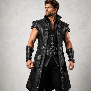 Puede incluir: Un abrigo largo negro sin mangas con tachuelas plateadas, múltiples hebillas y un bolsillo lateral, sobre una camisa y pantalones negros. El conjunto incluye muñequeras negras a juego y botas altas con cordones y varias hebillas.