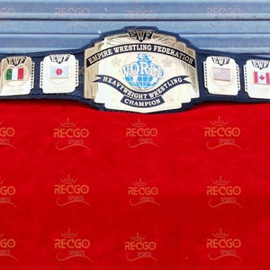 Puede incluir: Un cinturón de campeonato de lucha libre profesional con una correa de cuero azul marino. La placa central dorada dice "EMPIRE WRESTLING FEDERATION WORLD HEAVYWEIGHT CHAMPION". Se muestran banderas de Italia, Japón, Estados Unidos y Canadá.