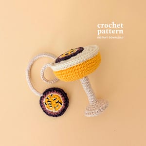 May include: A handmade crochet cocktail toy in yellow, white, and purple. The toy has a circular base and a stem, with a matching coaster attached by a crocheted cord. The text "crochet pattern INSTANT DOWNLOAD" is visible.