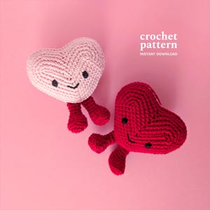 May include: Two crocheted heart-shaped toys with smiling faces and small legs. One is light pink, the other is red. The background is a solid pink. Text on the image reads "crochet pattern" and "instant download".