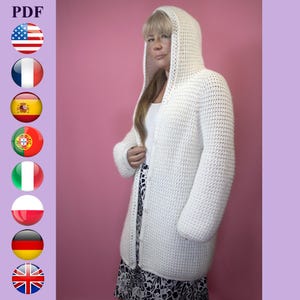 Puede incluir: Un cárdigan blanco con capucha de ganchillo con mangas largas. El suéter abierto está hecho de un punto texturizado y llega a la rodilla. La modelo lleva un top blanco y una falda estampada en blanco y negro. El fondo es rosa liso.