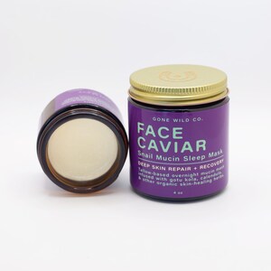 Może przedstawiać: Dwa słoiki Face Caviar Snail Mucin Sleep Mask. Jeden słoik jest otwarty, ukazując kremową substancję. Drugi słoik jest zamknięty złotą pokrywką. Etykieta jest fioletowa z białym i zielonym tekstem. Słoik zawiera 118 ml.