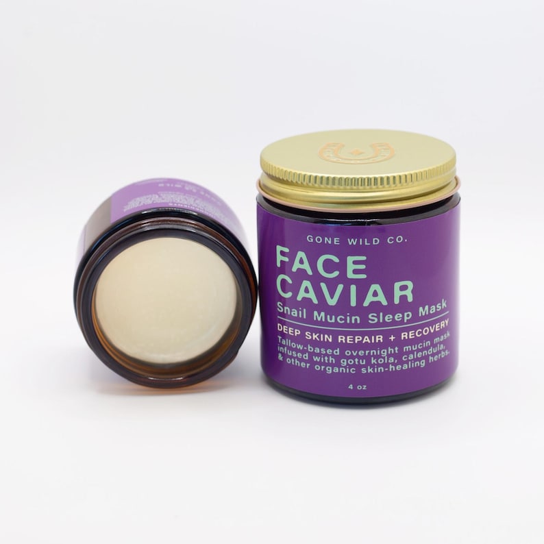 Może przedstawiać: Dwa słoiki Face Caviar Snail Mucin Sleep Mask. Jeden słoik jest otwarty, ukazując kremową substancję. Drugi słoik jest zamknięty złotą pokrywką. Etykieta jest fioletowa z białym i zielonym tekstem. Słoik zawiera 118 ml.