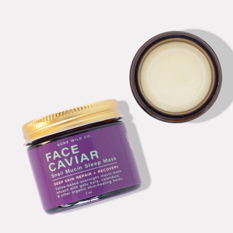 Może przedstawiać: Słoik Face Caviar Snail Mucin Sleep Mask ze złotą pokrywką i fioletową etykietą. Etykieta zawiera tekst "GONE WILD CO." i szczeg&oacute;ły produktu. Otwarty słoik maski znajduje się obok. Produkt ma 59 ml.
