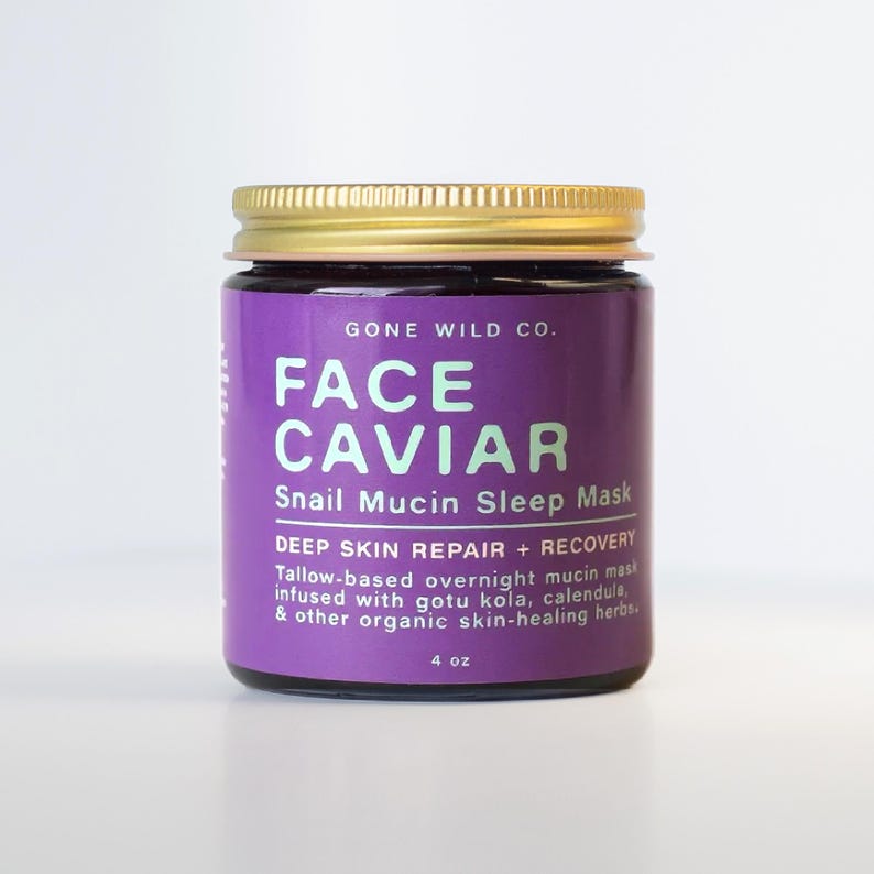 Może przedstawiać: Słoik Face Caviar Snail Mucin Sleep Mask firmy Gone Wild Co. Słoik ma złotą pokrywkę i fioletową etykietę z białym tekstem. Etykieta głosi "Face Caviar" i "Snail Mucin Sleep Mask". Słoik zawiera 118 ml produktu.