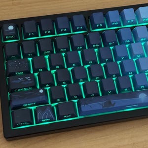 May include: A mechanical keyboard with dark blue and light blue keycaps. The keys are backlit with a green glow. The keyboard has a black frame and a standard QWERTY layout. The keycaps have white lettering and symbols.