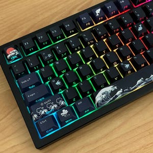 May include: Black mechanical keyboard with backlit keys. The keyboard features custom keycaps with wave and mountain designs. The keys are illuminated with a rainbow gradient, and the keyboard has a wooden frame.