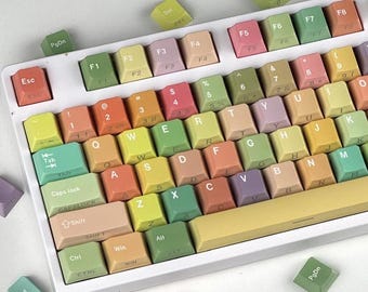 May include: A white mechanical keyboard with colorful keycaps in shades of pink, yellow, green, and orange. The keycaps are scattered around the keyboard. The keyboard has a yellow space bar and a variety of function keys.