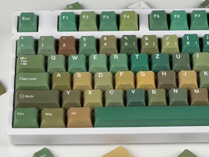 May include: A close-up of a mechanical keyboard with green and brown keycaps. The keyboard has a white frame and a variety of keys, including function keys, letters, numbers, and symbols. The keycaps are in various shades of green and brown.