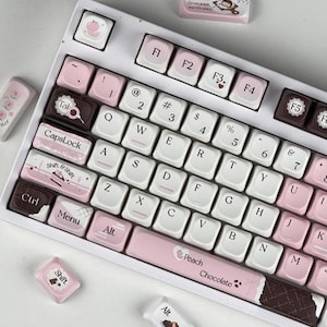 Puede incluir: Un teclado mecánico blanco con teclas personalizadas en tonos rosa, marrón y blanco. Las teclas presentan varios diseños, incluido un tema de melocotón y chocolate, y el texto "Peach Chocolate". El teclado tiene una distribución QWERTY estándar.