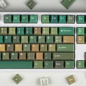May include: A mechanical keyboard with green and tan keycaps. The keyboard has a white frame and a variety of keys, including function keys, letters, numbers, and symbols. Some keycaps are scattered around the keyboard.