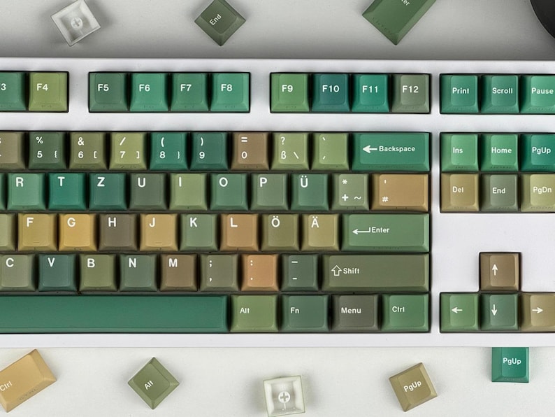 May include: A mechanical keyboard with green and tan keycaps. The keyboard has a white frame and a variety of keys, including function keys, letters, numbers, and symbols. Some keycaps are scattered around the keyboard.