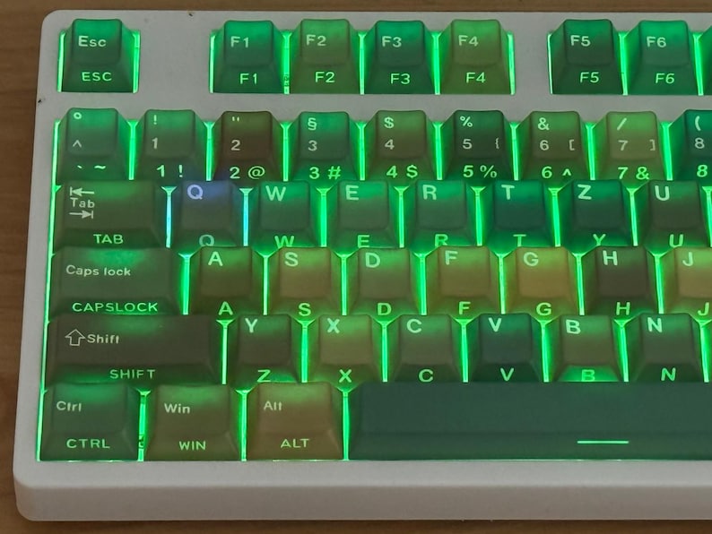 May include: A close-up of a white mechanical keyboard with green backlighting. The keycaps are a mix of colors, including green, brown, and yellow. The keyboard has function keys and number keys.