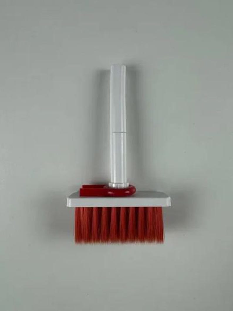 May include: A small, handheld cleaning brush with a white handle and a rectangular head. The brush head features vibrant red bristles. A red plastic piece connects the handle to the brush head.