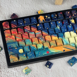 Może przedstawiać: Niestandardowa klawiatura mechaniczna z kolorowymi nakładkami na klawisze. Nakładki na klawisze mają żywy, artystyczny wzór z gradientem kolorów, w tym niebieskiego, pomarańczowego i żółtego, przypominający gwiaździste niebo. Klawiatura jest na neutralnym tle.
