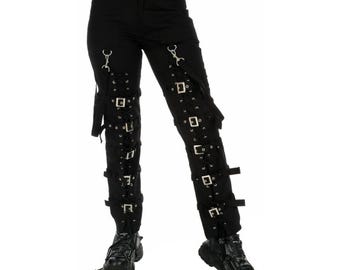 May include: Black pants with multiple silver buckles and straps running down the legs. The pants have a high waist and are paired with black boots. The overall style is edgy and alternative.