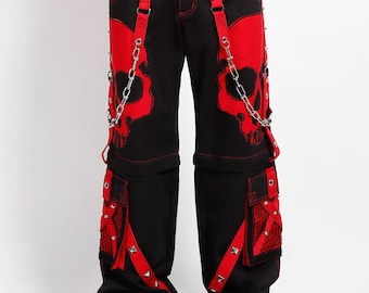 Puede incluir: Pantalones negros con diseños de calaveras rojas en la parte delantera. Los pantalones presentan detalles rojos, correas y bolsillos con tachuelas plateadas. Cadenas cuelgan de las correas. Cintura con cordón y botas de plataforma negras.