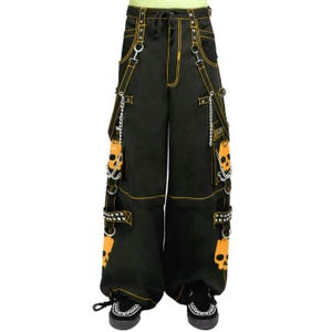 Può includere: Pantaloni cargo neri con cuciture gialle e dettagli a teschio. I pantaloni presentano più tasche, catene e cinghie decorative. Il design include grafiche di teschi arancioni e hardware argentato.