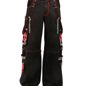 May include: Black pants with red stitching and accents. The pants feature multiple pockets, chains, and straps. The design includes red fabric panels and silver hardware. The pants have a wide leg opening and a drawstring waist.