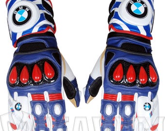 Puede incluir: Par de guantes de moto azules, blancos y rojos con el logo de BMW. Los guantes presentan detalles rojos en los nudillos y dedos, con un diseño a rayas azules y blancas en los puños. Fabricados en cuero, ofrecen protección.