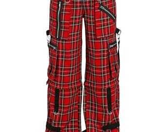 May include: Red plaid cargo pants with black accents, zippers, and straps. The pants have multiple pockets and a drawstring waist. The fabric features a black and white grid pattern over a red background. The pants are worn with black platform shoes.