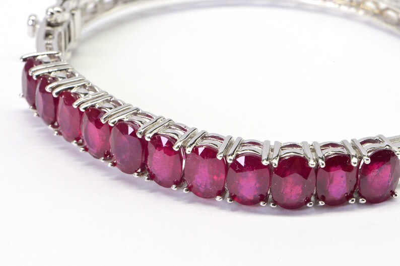 May include: A silver bracelet with a row of oval-shaped ruby gemstones.
