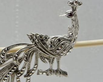 Puede incluir: Un broche de pavo real de plata con un ojo de piedra roja y un diseño detallado de piedras de marcasita.